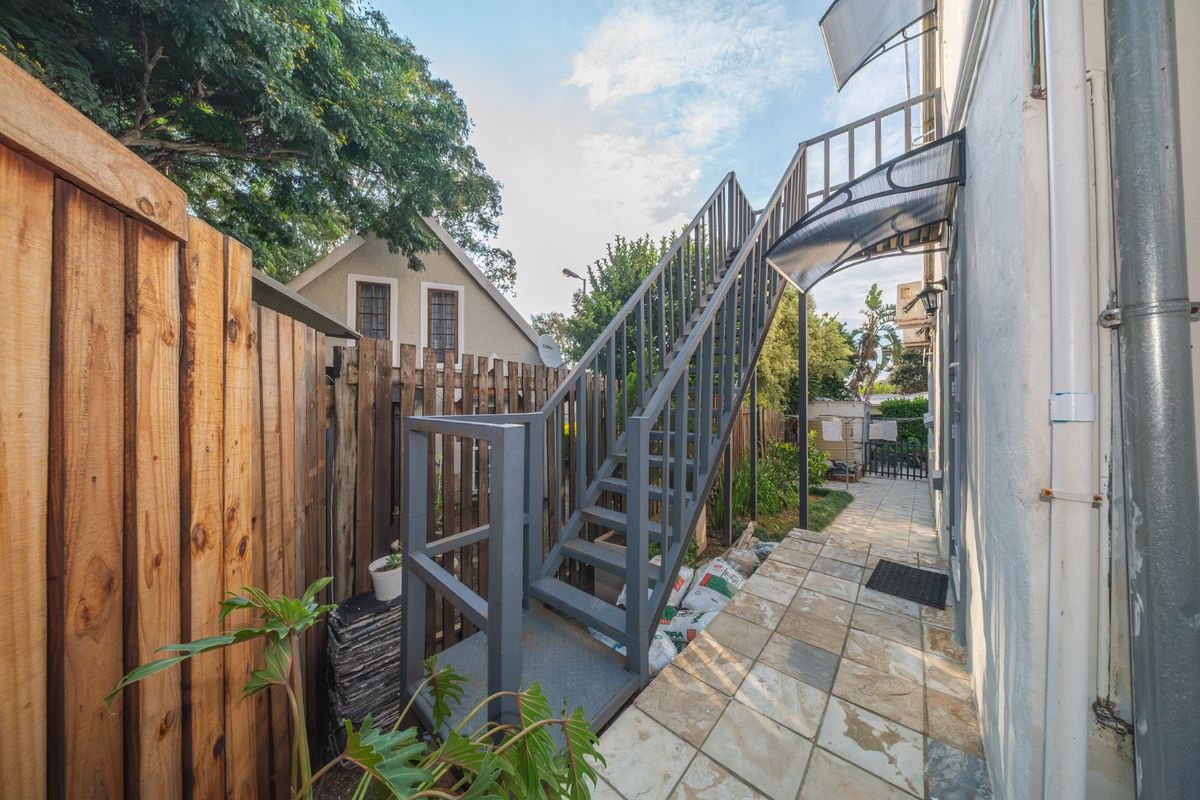 Rear exterior view of the property featuring a metal staircase leading to an upper level, stone tiled patio, and wooden perimeter fencing.