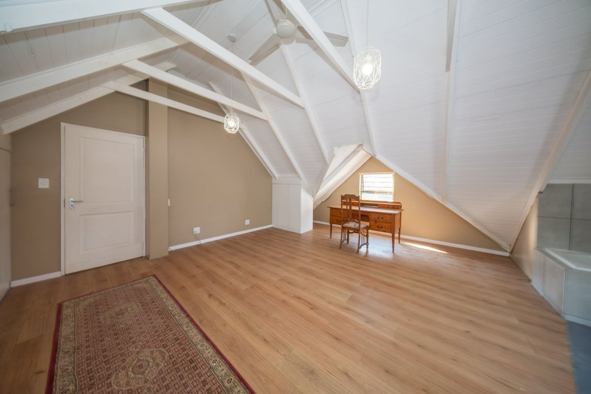 Spacious attic-style bedroom featuring exposed white timber rafters, laminate flooring, and built-in storage, offering a bright and versatile living space.