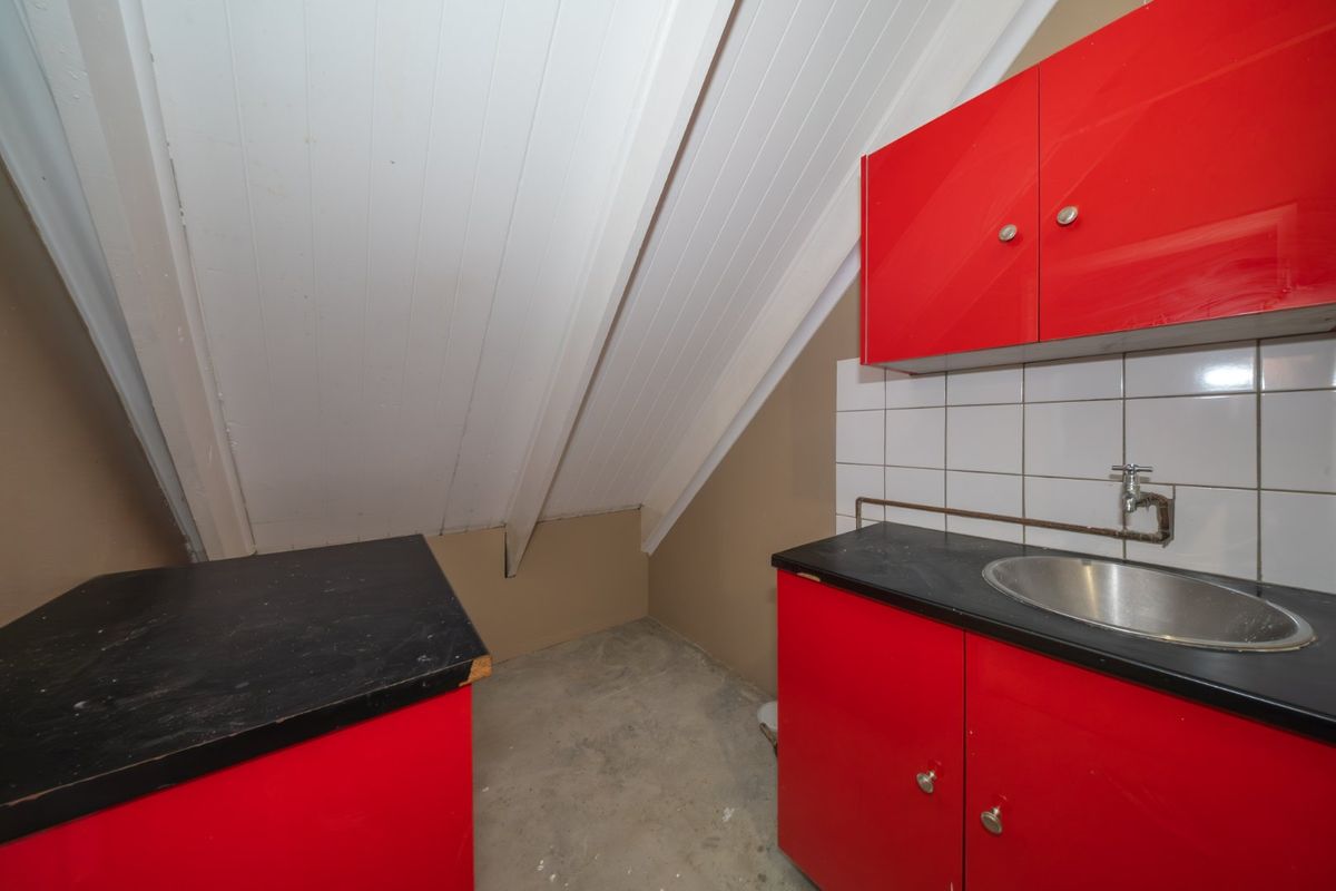 A compact kitchen area featuring red cabinetry, a stainless steel sink, and a sloped ceiling, currently requiring cosmetic updates and flooring installation.