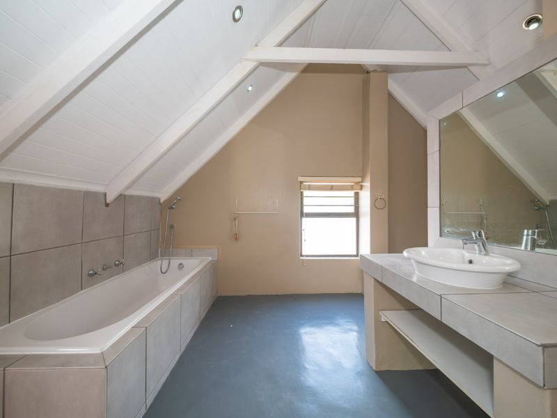 Spacious attic-style bathroom featuring a built-in bathtub, tiled vanity with vessel sink, and exposed timber ceiling beams.