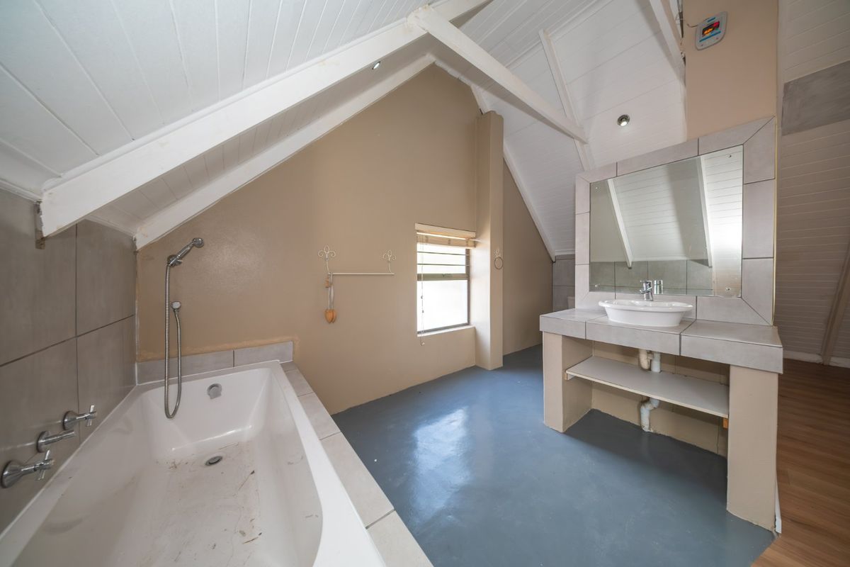 A spacious attic-style bathroom featuring a built-in bathtub, a tiled vanity with a vessel sink, and exposed ceiling beams.