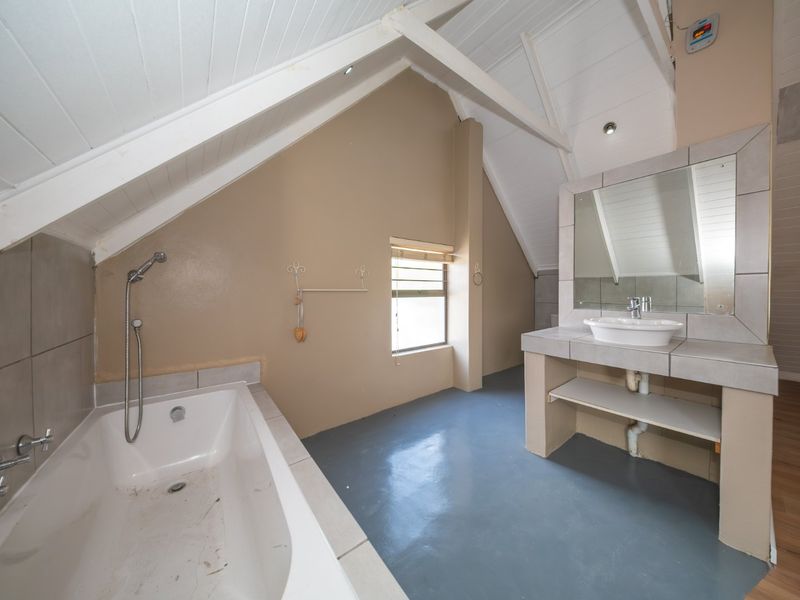 A spacious attic-style bathroom featuring a built-in bathtub, a tiled vanity with a vessel sink, and exposed ceiling beams.