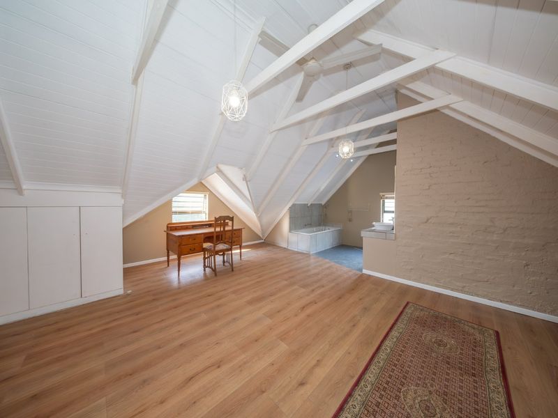 Spacious attic-style bedroom featuring vaulted ceilings with exposed rafters, laminate flooring, built-in storage, and an integrated bathtub area.