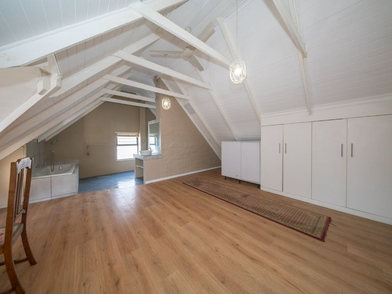 Spacious attic-style bedroom featuring vaulted ceilings with exposed beams, built-in storage, laminate flooring, and an integrated en-suite bathroom area.