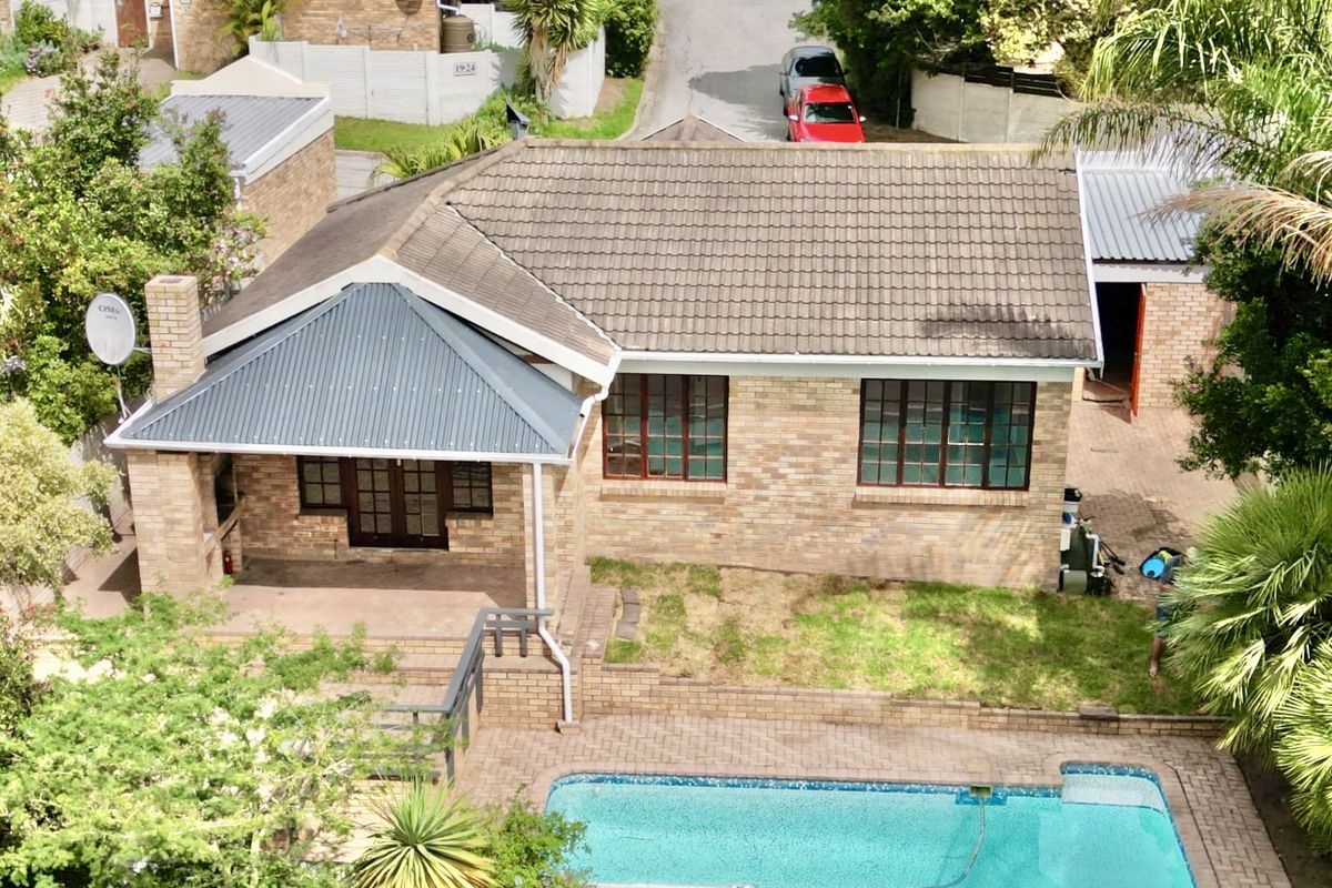 Aerial view of a brick house featuring a tiled roof, a swimming pool, and a paved patio area in a residential setting.