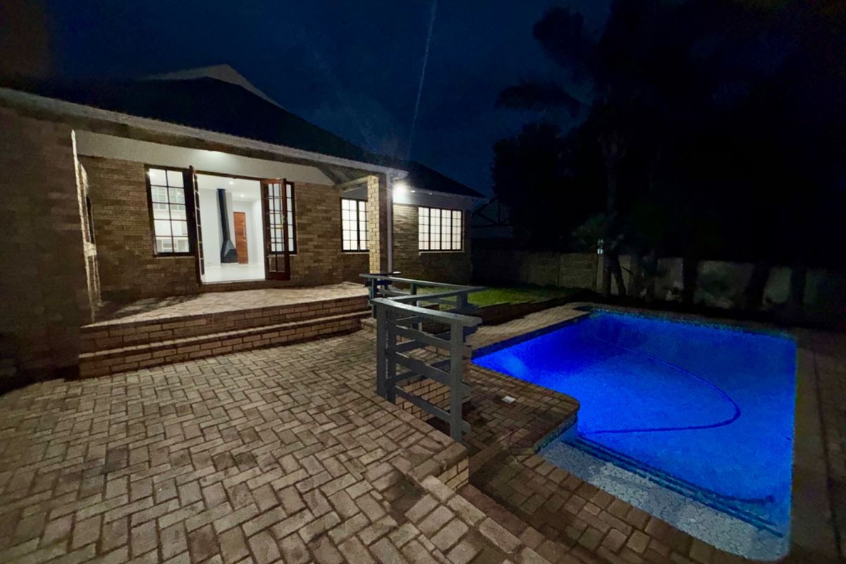 Night view of the rear exterior featuring a brick-paved patio, swimming pool, and direct access to the interior through french doors.