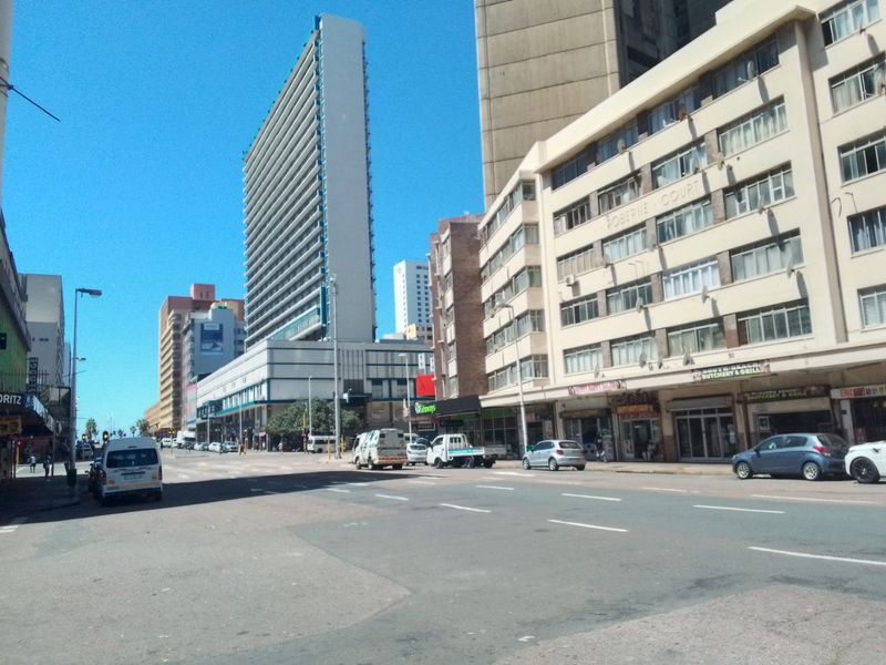 A street-level view of a busy urban area featuring multi-story apartment buildings and commercial storefronts along the road.