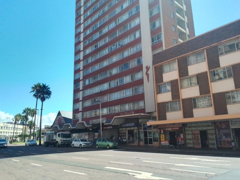 Street-level view of a multi-story apartment building featuring ground-floor retail spaces and a prominent facade in an urban setting.