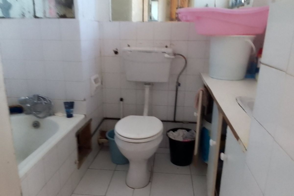 A dated bathroom featuring a bathtub, toilet, and vanity unit with tiled surfaces, currently requiring maintenance and cosmetic updates.
