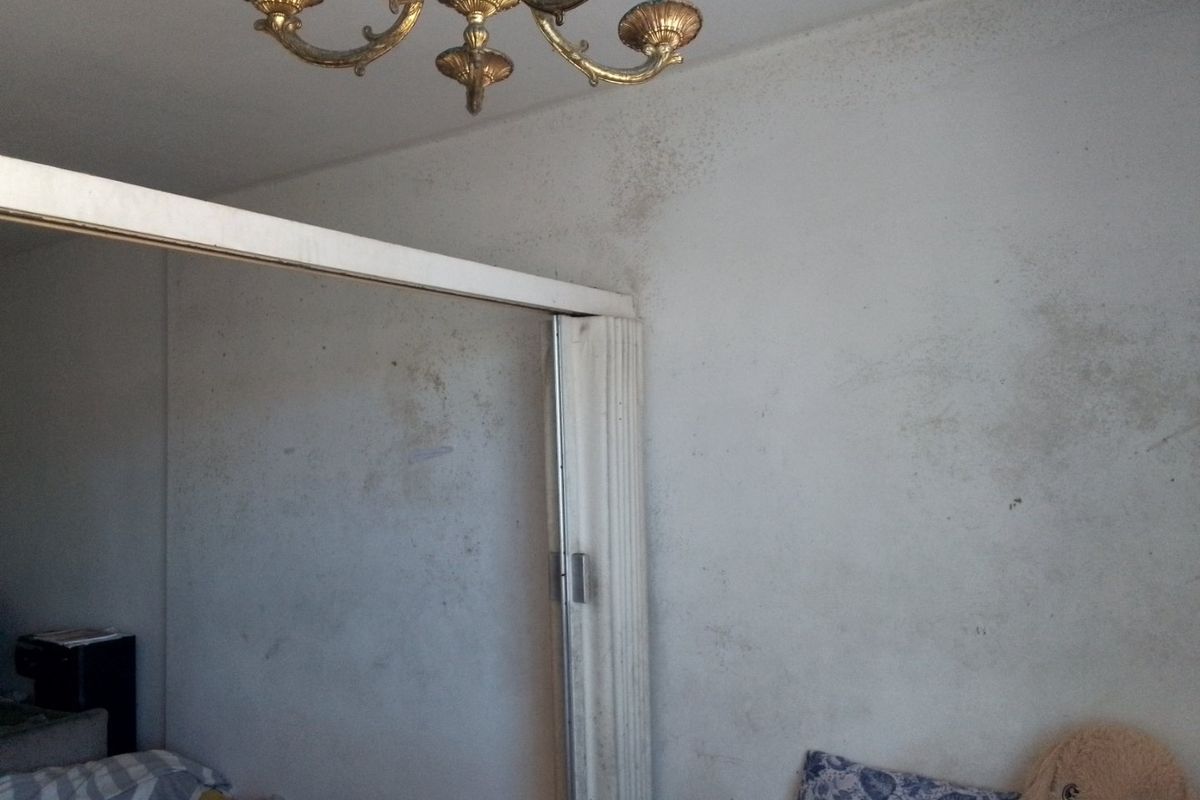 Bedroom interior featuring a classic chandelier and a sliding room divider, showing significant wall surface deterioration and staining.