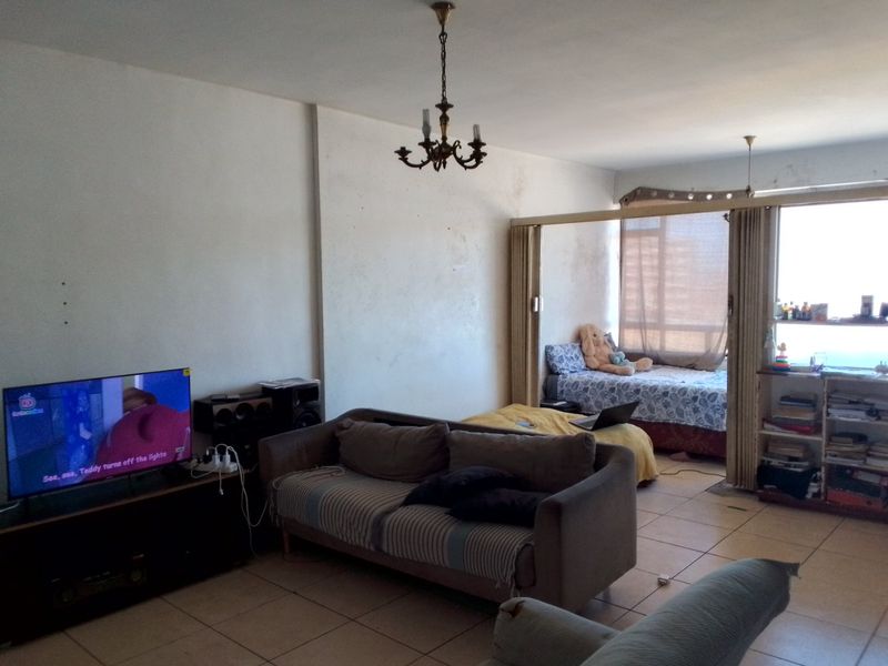 Open-plan living area featuring ceramic floor tiles, a sliding room divider, and a large window, requiring cosmetic updates to the walls and ceiling.