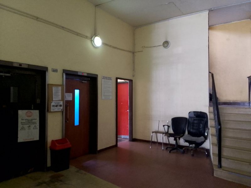 Communal apartment building lobby featuring elevator access, a staircase with a metal handrail, and basic wall-mounted lighting fixtures.