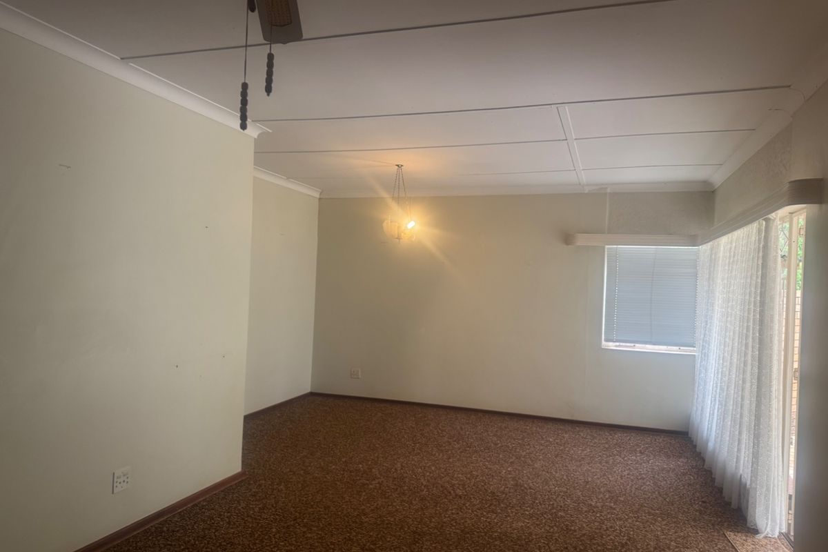 An empty living room featuring carpet flooring, a ceiling fan, and sliding glass doors leading to the exterior.