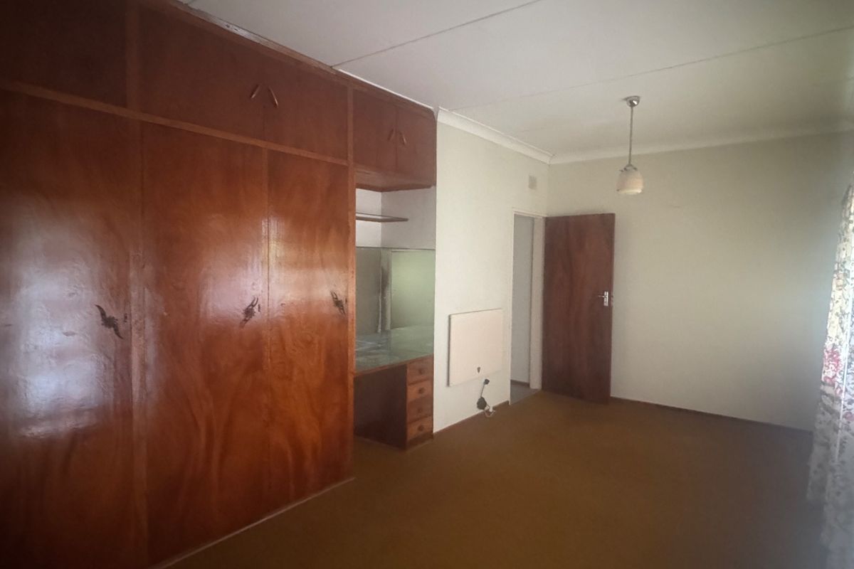 A spacious bedroom featuring extensive built-in wooden cabinetry, a vanity area, and carpeted flooring, offering a blank canvas for modernization.