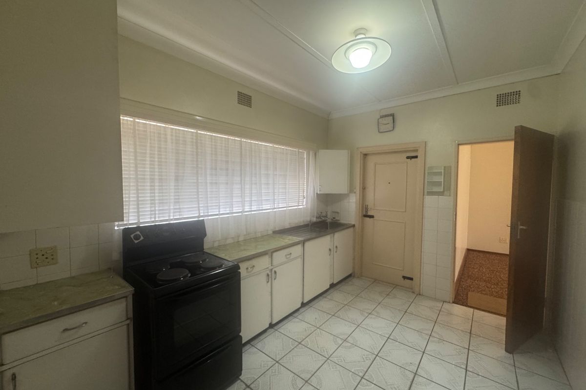 A functional kitchen featuring dated cabinetry, laminate countertops, an electric stove, and tiled flooring, offering potential for a modern renovation.