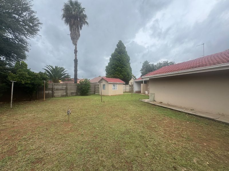 Spacious rear garden featuring a lawn, concrete pathway, perimeter boundary wall, and a small detached outbuilding with a matching tiled roof.