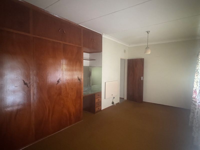 A spacious bedroom featuring extensive built-in wooden cabinetry, a vanity area, and carpeted flooring, offering a blank canvas for modernization.