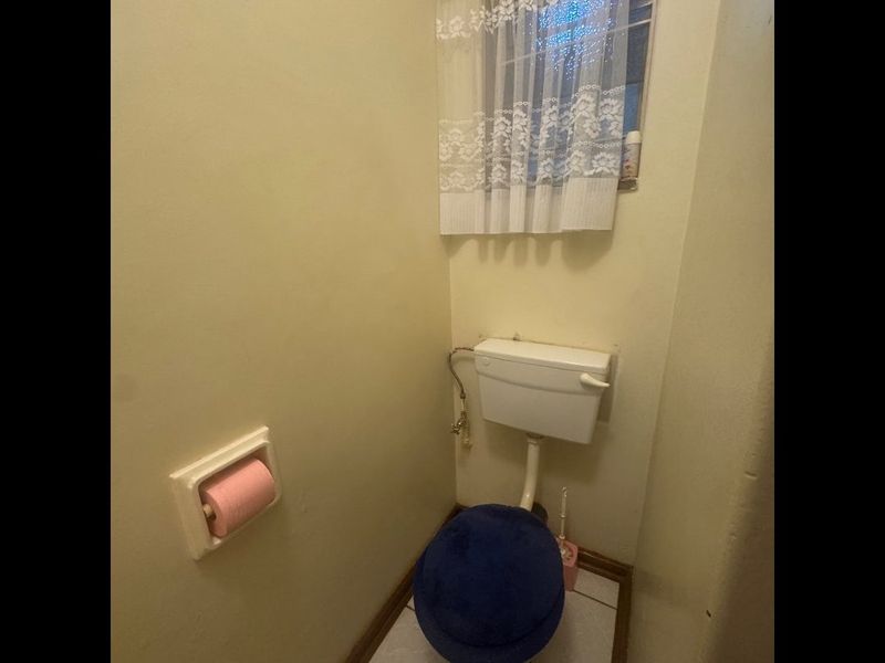 A compact bathroom featuring a standard toilet and tiled flooring, currently showing signs of age and wear.