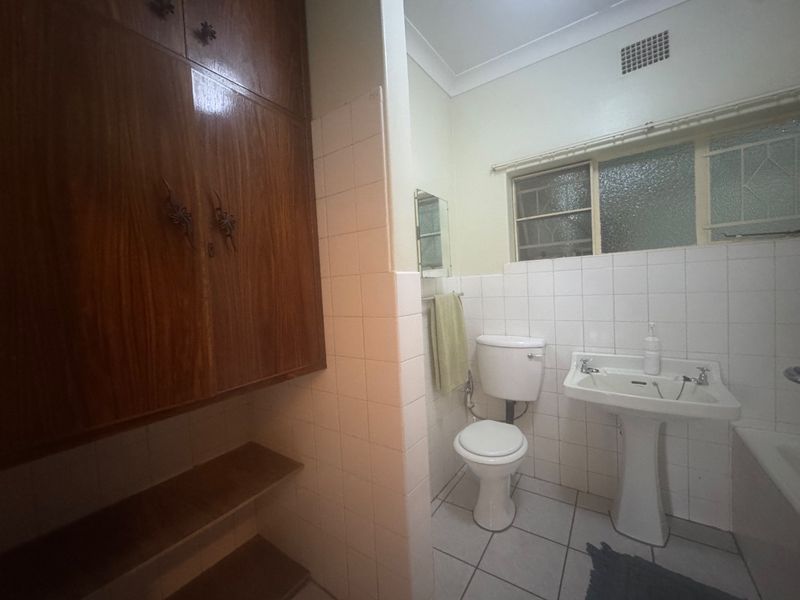 A functional bathroom featuring a pedestal basin, toilet, and built-in wooden storage cabinetry with tiled finishes.