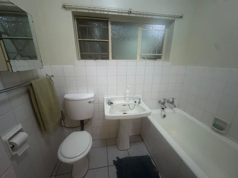 A functional bathroom featuring a pedestal basin, bathtub, and toilet with tiled finishes, offering potential for modernization and cosmetic updates.