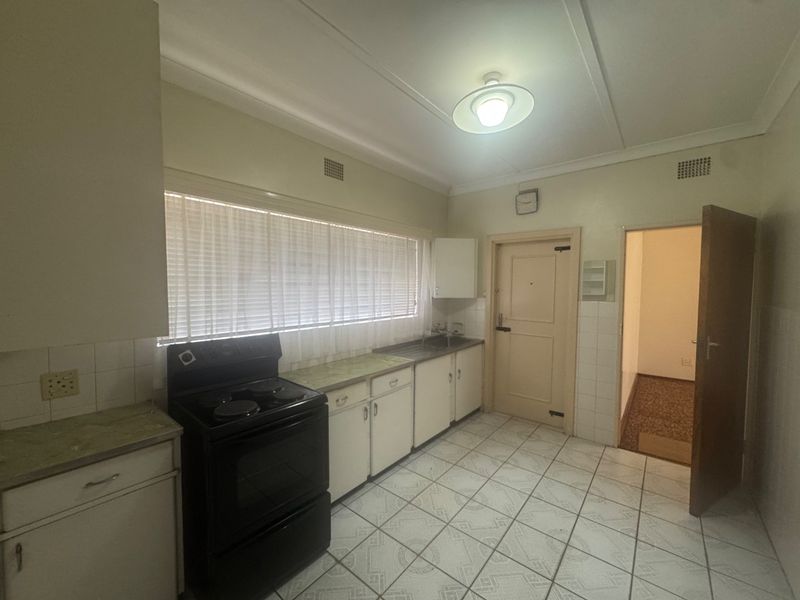 A functional kitchen featuring dated cabinetry, laminate countertops, an electric stove, and tiled flooring, offering potential for a modern renovation.