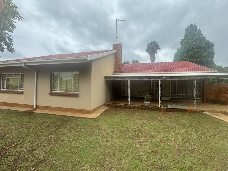 Rear view of the house featuring a tiled roof, brick chimney, and a covered patio area overlooking the garden.