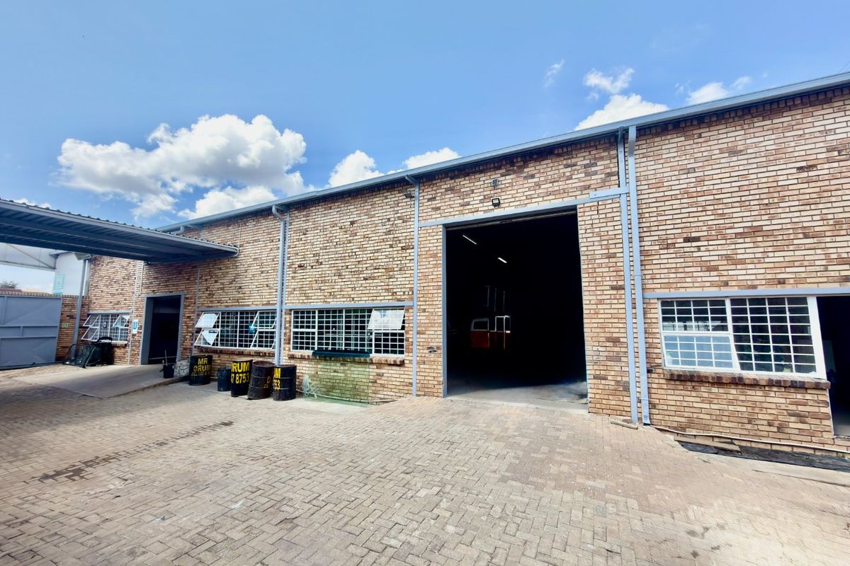 Commercial industrial property featuring a face brick facade, paved driveway, steel security bars, and a large roller shutter entrance.
