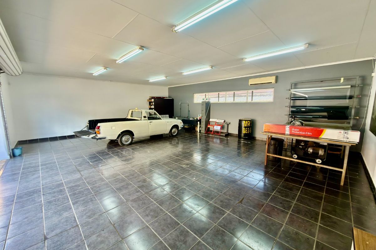 Spacious commercial garage featuring durable tiled flooring, bright fluorescent lighting, and a wall-mounted air conditioning unit, suitable for workshop or storage use.
