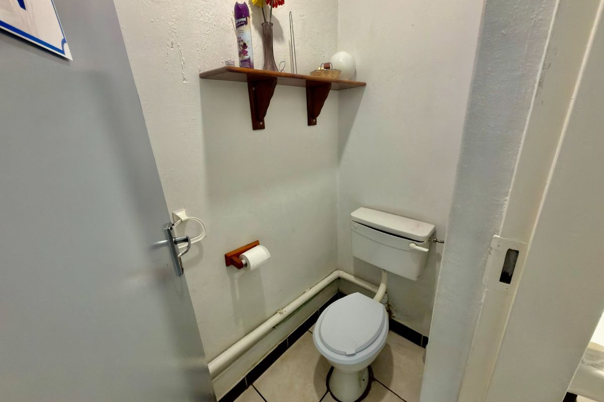 A compact commercial bathroom featuring a standard toilet, wall-mounted shelving, and exposed plumbing, requiring cosmetic updates to improve the overall finish.