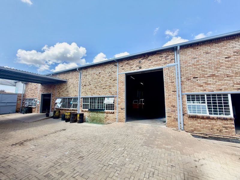 Commercial industrial property featuring a face brick facade, paved driveway, and large roller shutter access point with steel security window bars.