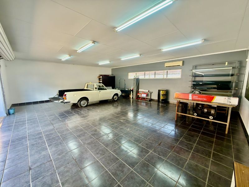 Spacious commercial garage featuring tiled flooring, fluorescent lighting, and a wall-mounted air conditioning unit, suitable for workshop or storage use.