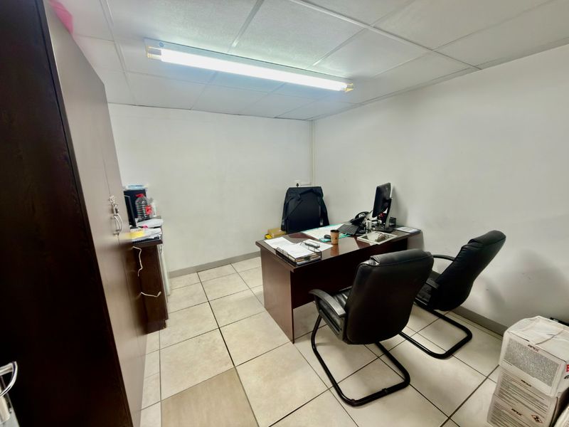 A functional commercial office space featuring tiled flooring, a suspended ceiling, and integrated fluorescent lighting.