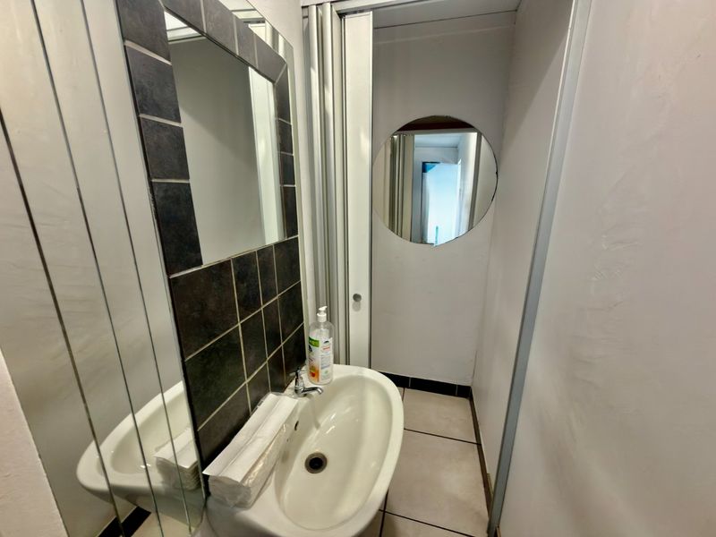 A compact commercial bathroom featuring a wall-mounted basin, tiled splashback, and tiled flooring, requiring minor maintenance and cosmetic updates.