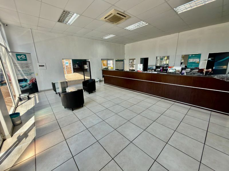 Commercial reception area featuring a large built-in service counter, tiled flooring, and suspended ceiling with integrated lighting and air conditioning.