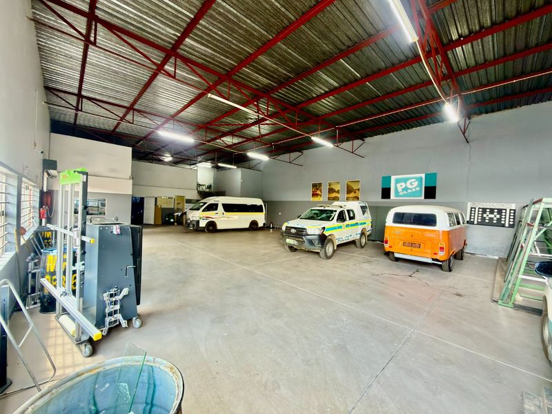 Spacious commercial garage or workshop area featuring high ceilings with exposed steel trusses, concrete flooring, and ample open floor space for vehicle storage.