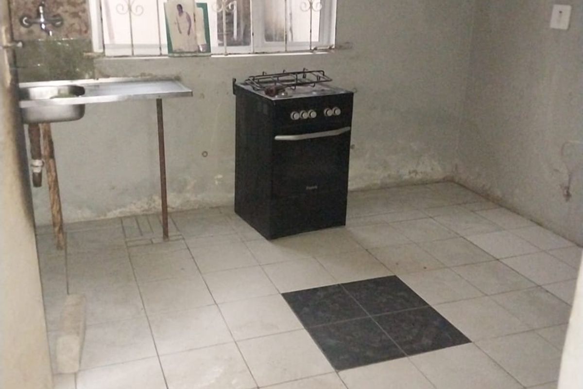 A basic, unfinished kitchen area featuring a simple sink, a freestanding stove, and tiled flooring with some missing tiles.
