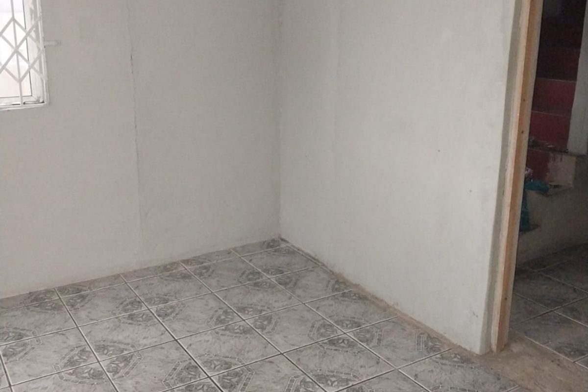 An empty, unfinished room featuring tiled flooring, a security-grille window, and an open doorway leading to an adjacent area.