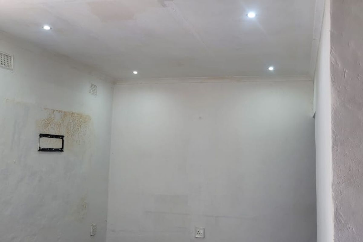 An empty interior room featuring recessed ceiling lighting, electrical outlets, and wall-mounted fixtures, requiring cosmetic updates to the wall surfaces.