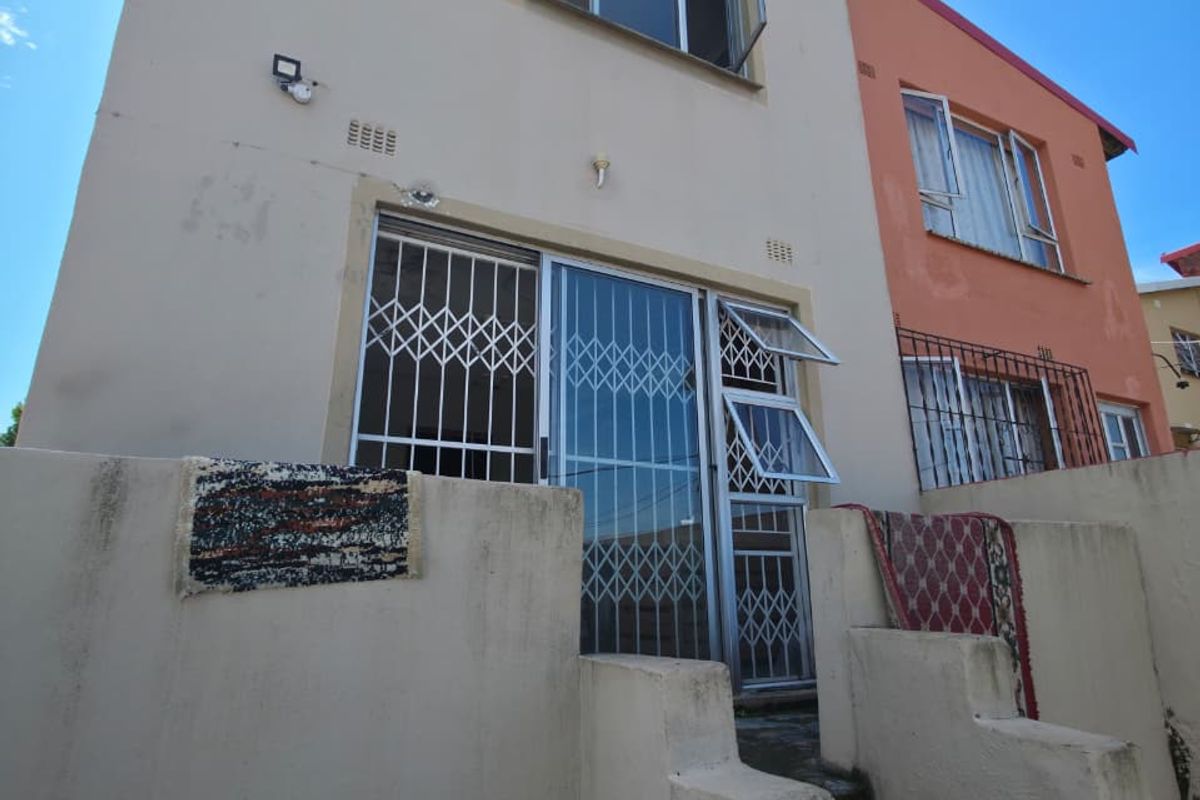 Rear exterior view of a multi-story residential building featuring security gates, metal-framed windows, and a concrete staircase leading to the entrance.
