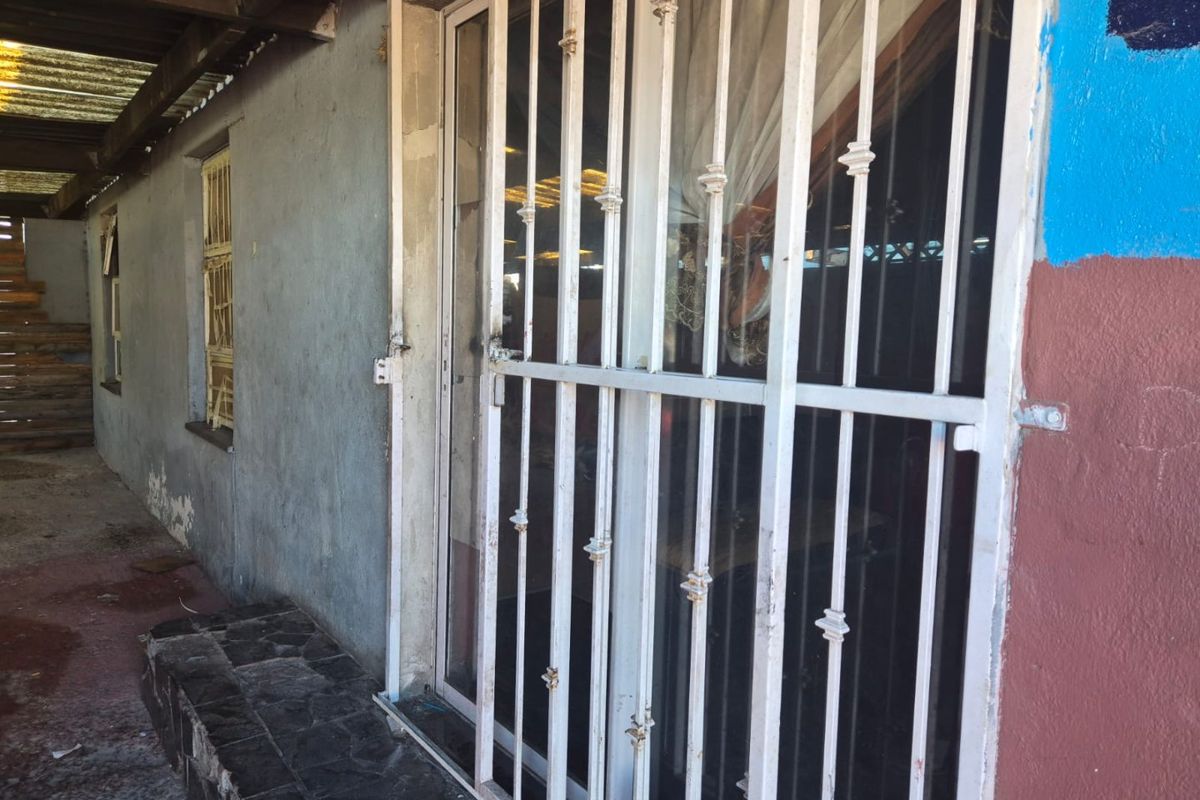 Exterior view of a rear patio area featuring a security gate, sliding door access, and weathered wall finishes.