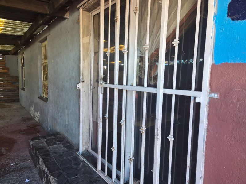 Exterior view of a rear patio area featuring a security gate, sliding door access, and weathered wall finishes.