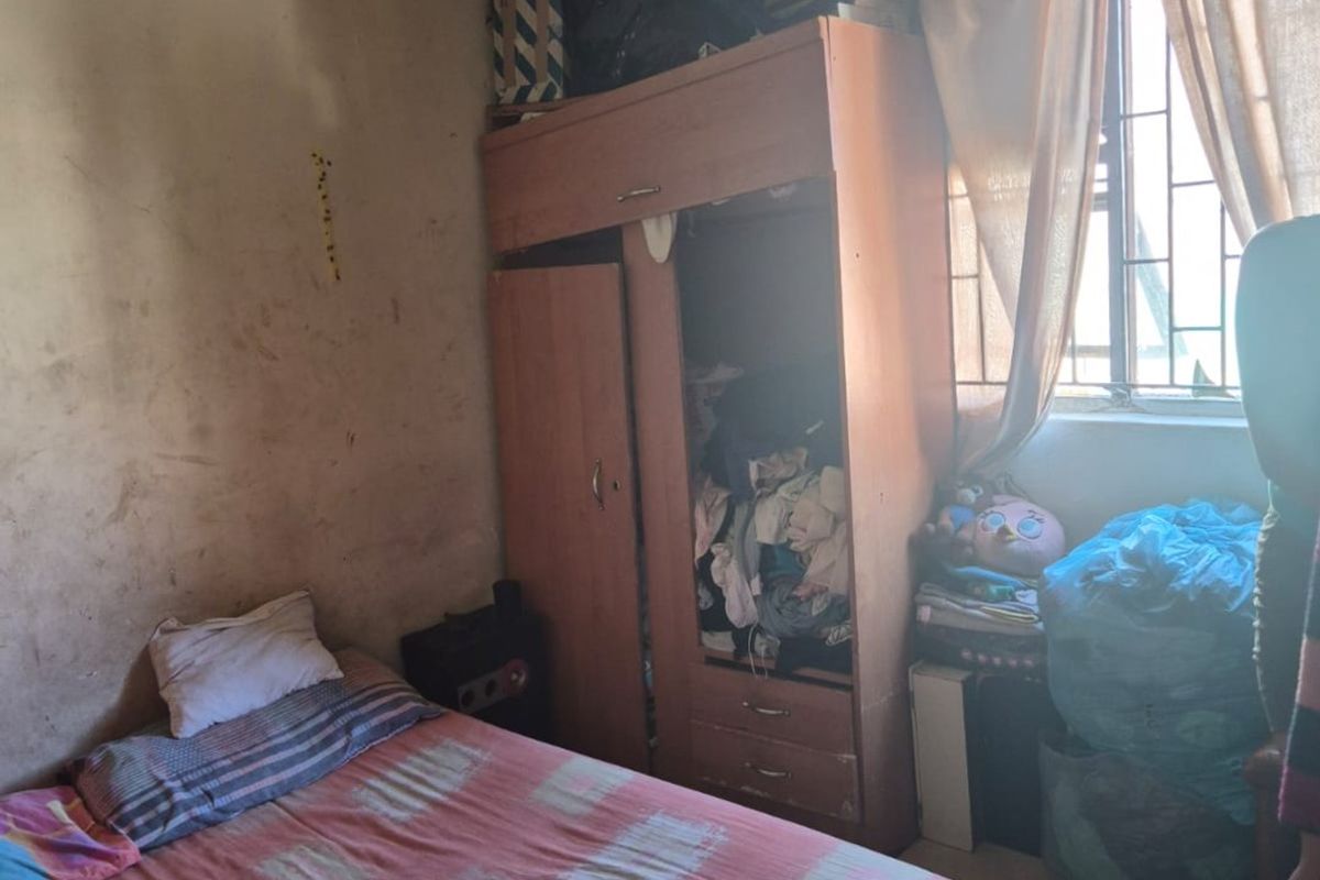 A bedroom featuring a built-in wardrobe and security bars on the window, currently requiring significant cosmetic updates and wall repairs.