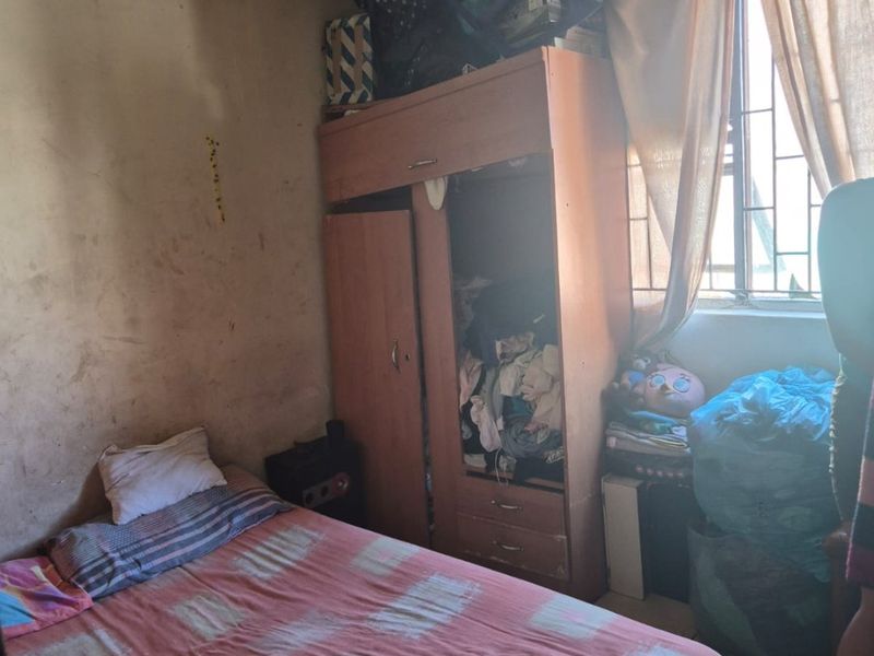 A bedroom featuring a built-in wardrobe and security bars on the window, currently requiring significant cosmetic updates and wall repairs.