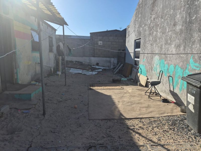 A rear exterior yard area featuring sandy ground, concrete block boundary walls, and weathered building facades in need of maintenance and landscaping.