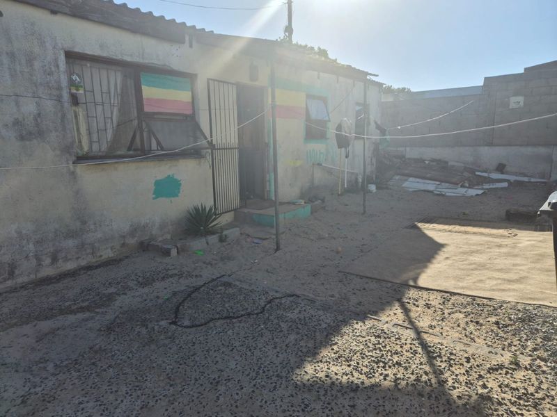 Rear exterior view of the property showing the building facade, security features, and an unpaved yard area requiring maintenance and landscaping.