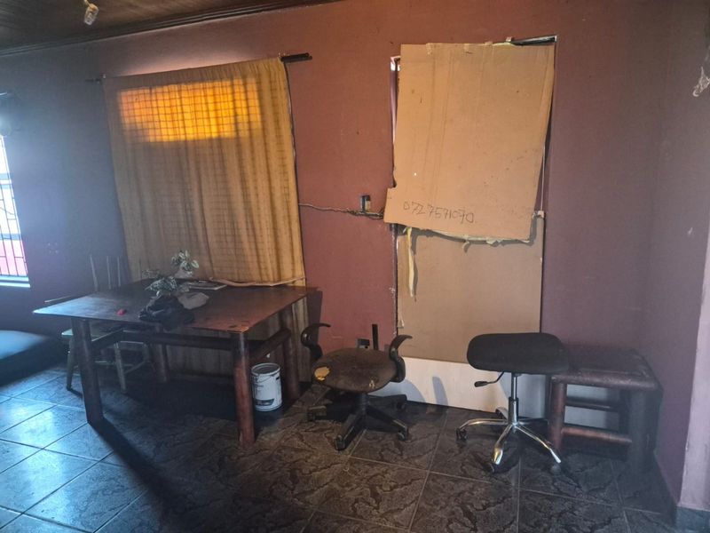 A living area featuring tiled floors and timber ceilings, currently requiring significant repairs to wall finishes and window fixtures.
