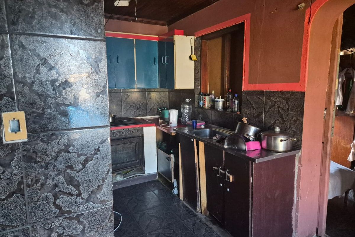 A dated kitchen featuring dark tiled splashbacks, built-in cabinetry, and a freestanding oven, requiring significant cosmetic updates and modernization.