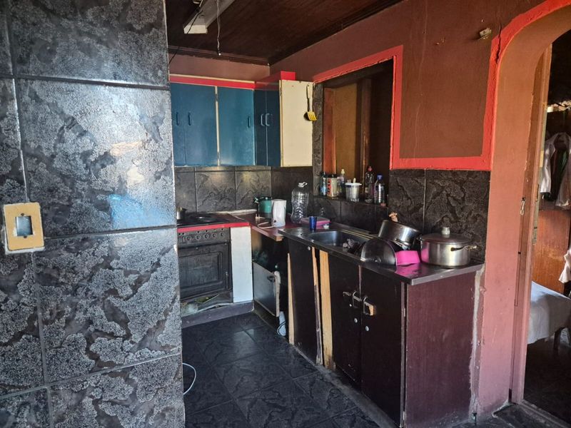 A dated kitchen featuring dark tiled splashbacks, built-in cabinetry, and a freestanding oven, requiring significant cosmetic updates and modernization.