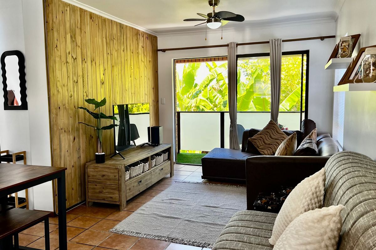 A comfortable living room featuring a wood panel accent wall, tiled flooring, and a ceiling fan, with direct access to a balcony.