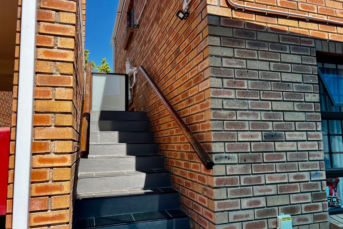 An exterior view of a brick apartment building featuring a tiled staircase with a wooden handrail leading to an upper level entrance.